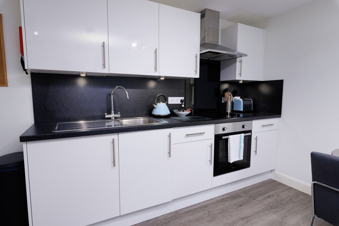A modern kitchen with white cabinets, a black countertop, a stainless steel sink, a kettle, and a toaster.