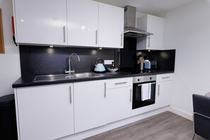 A modern kitchen with white cabinets, a black countertop, a stainless steel sink, a kettle, and a toaster. - Modern, Bright Studio in the Heart of Lerwick (Lerwick)