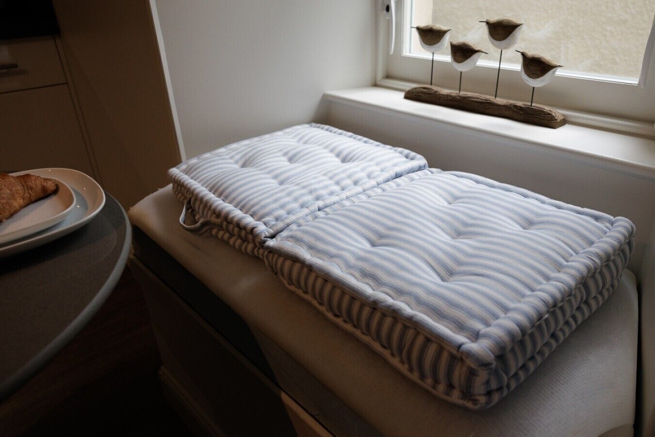 A neatly made bed with a striped pillow and a window sill with decorative bird figures.