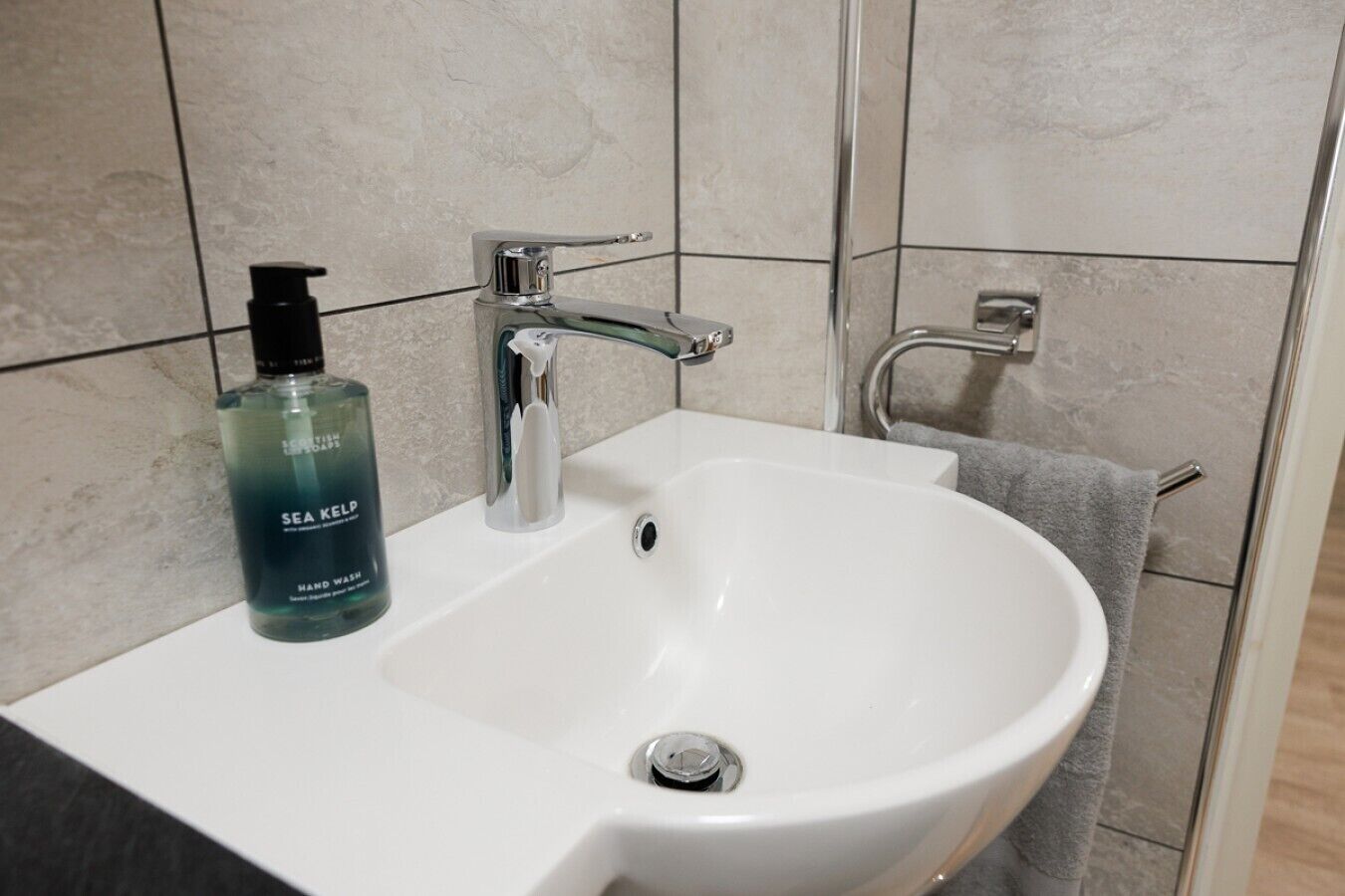 A bathroom with a white sink, a bottle of Sea Kelp hand wash, and a towel rack.