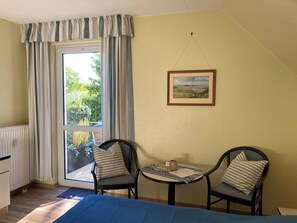 A room with a bed, a window with curtains, a table with chairs, and a framed picture on the wall. - Seaside air, expansive scenery, and time for yourselves—Strandstudio Strandhafer in Lobbe (Mönchgut)