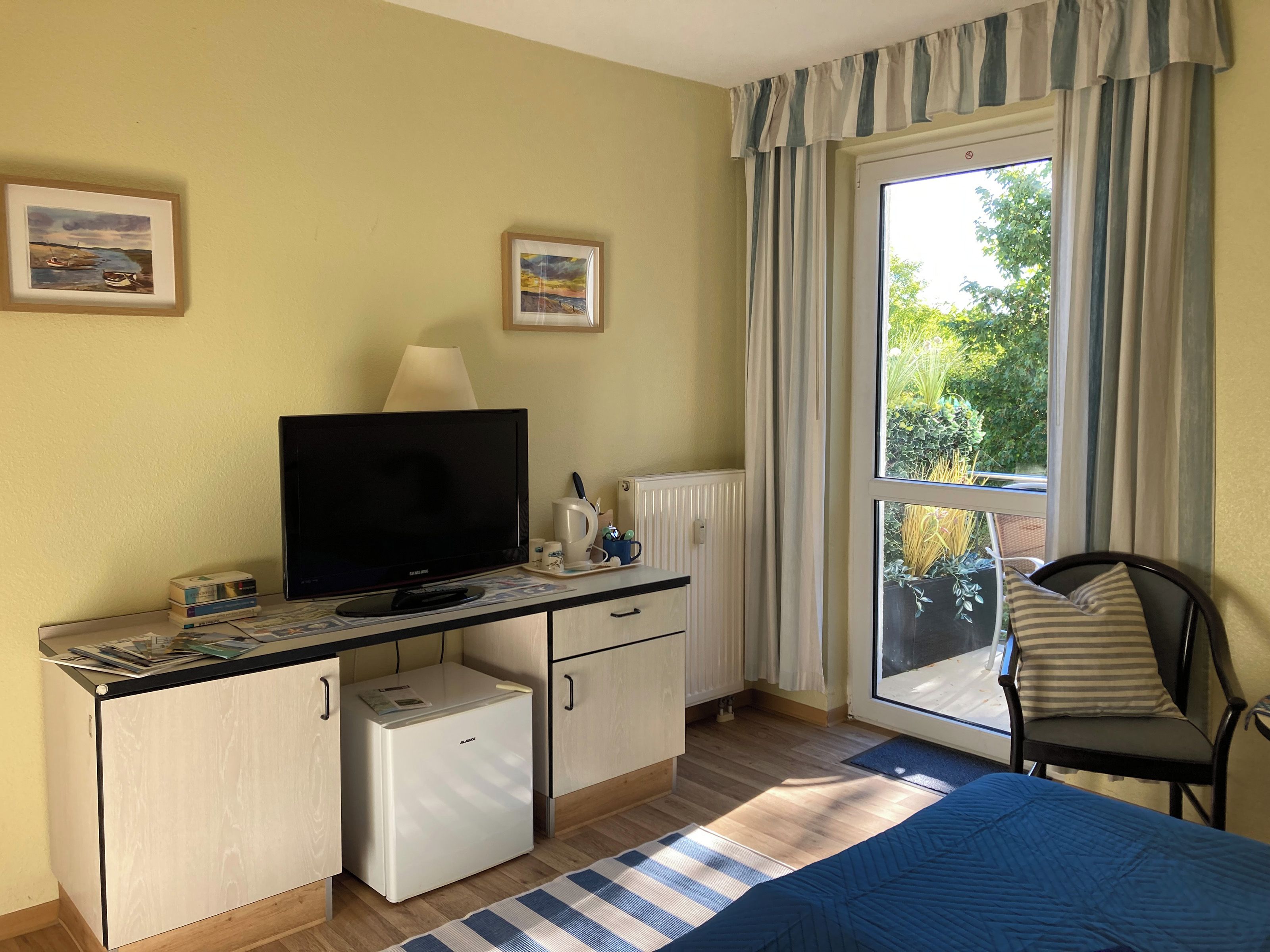 Ein Zimmer mit einem Bett, einem Schreibtisch mit Fernseher, einem kleinen Kühlschrank und einem Sessel.