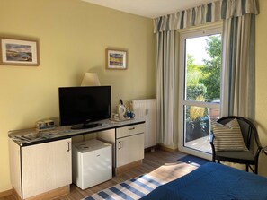 A room with a bed, a desk with a television, a small refrigerator, and a chair. - Seaside air, expansive scenery, and time for yourselves—Strandstudio Strandhafer in Lobbe (Mönchgut)