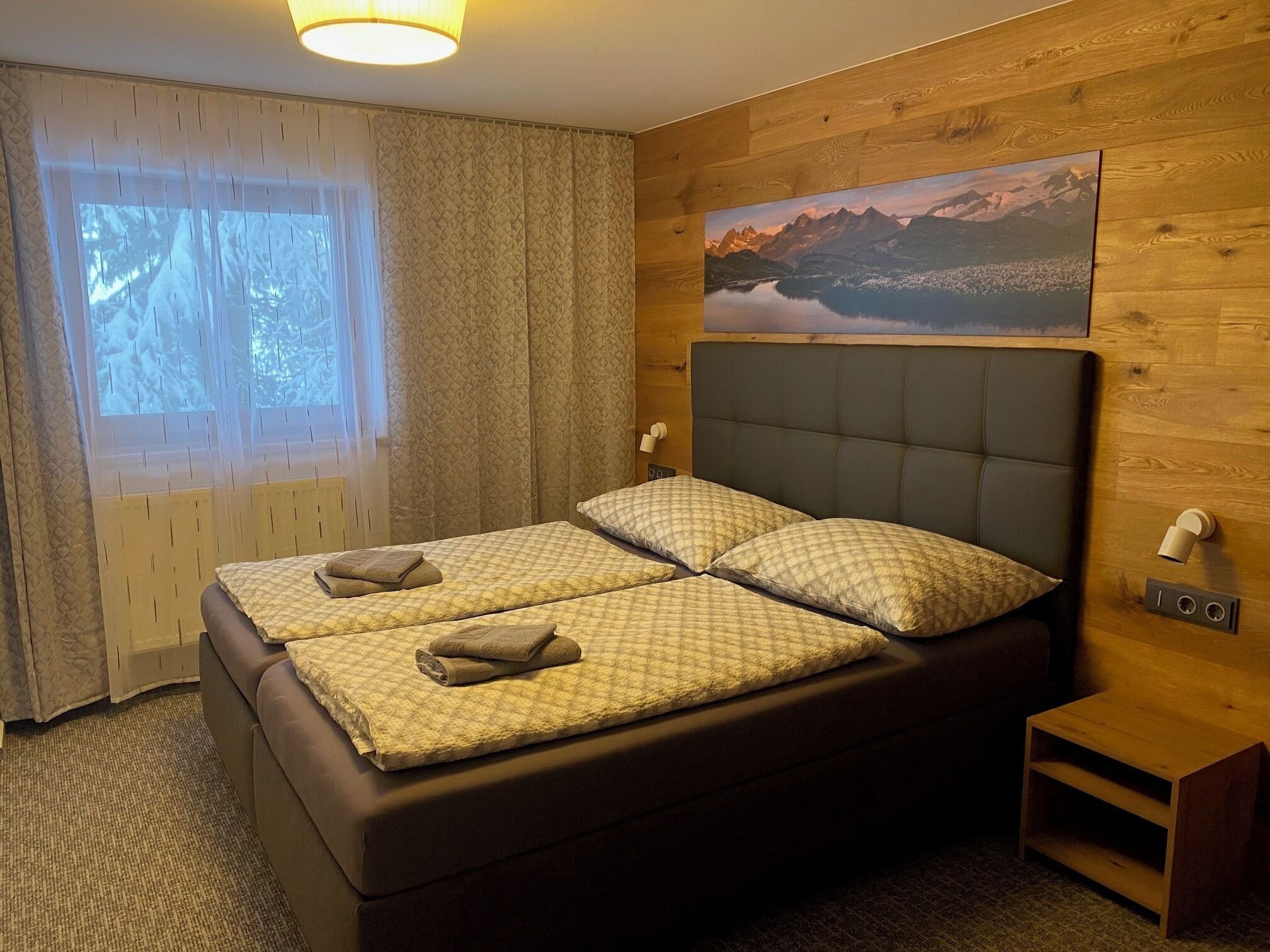 Ein Doppelbett mit gestepptem Kopfteil, zwei Kissen und ein Nachttisch mit Lampe.