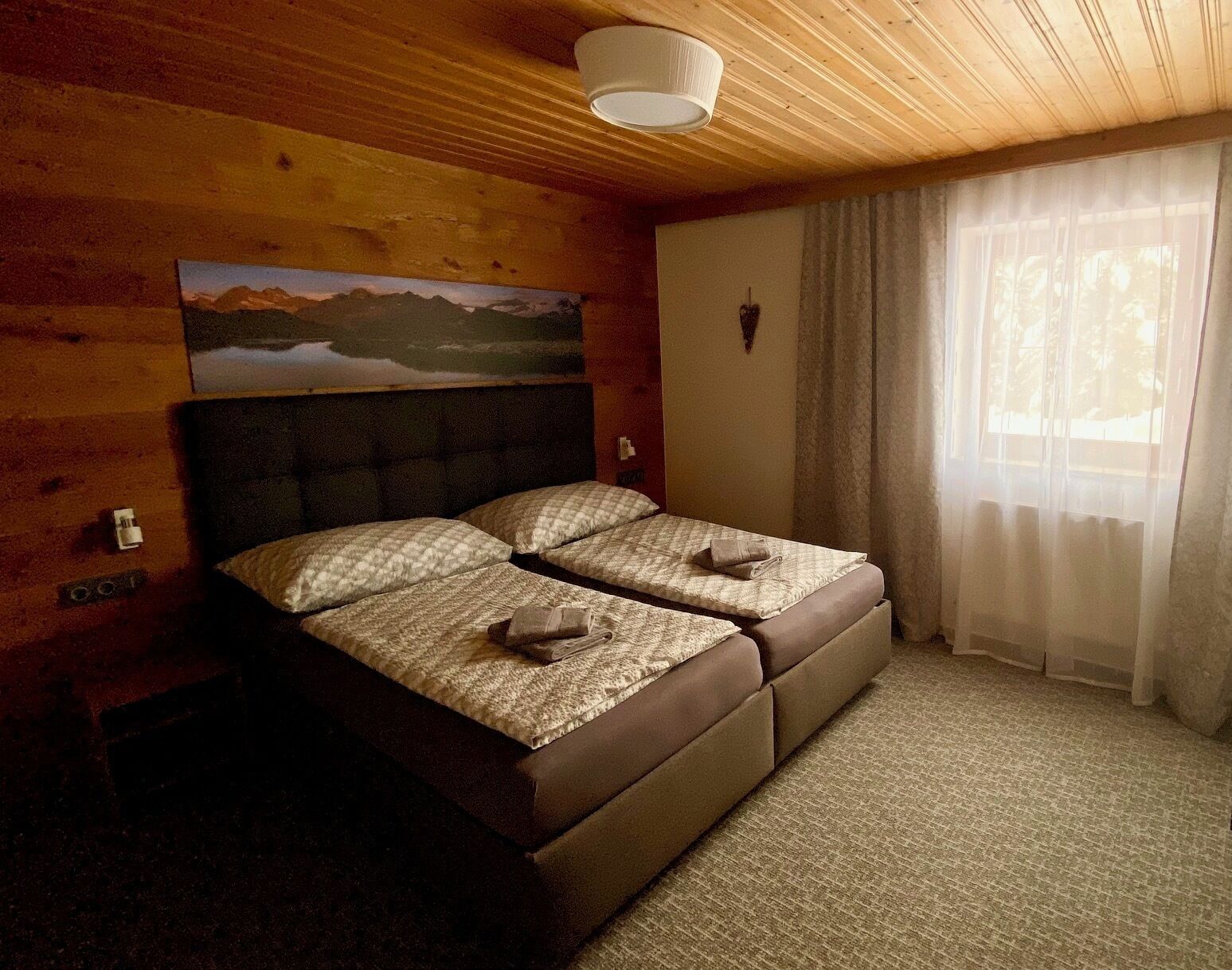 Una habitació amb un llit, un quadre a la paret i una finestra amb cortines.
