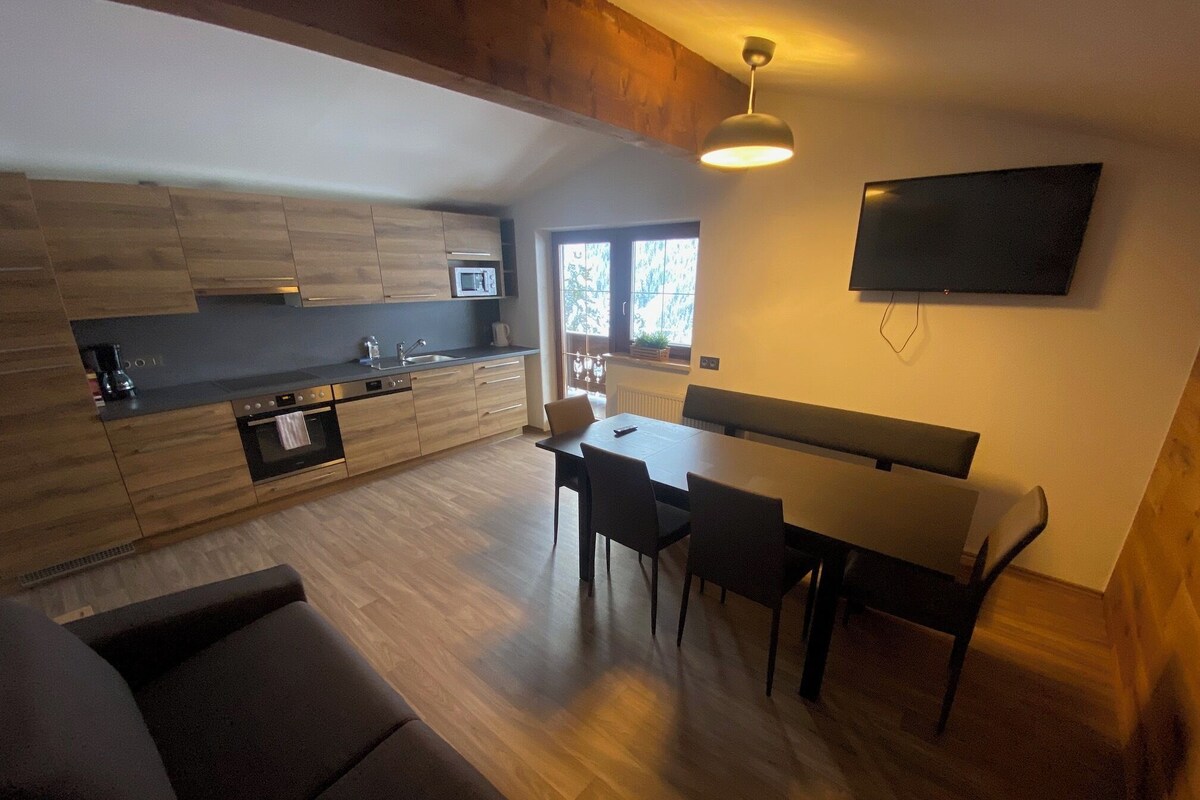 Una cocina moderna con comedor, televisor de pantalla plana en la pared y un amplio ventanal que proporciona luz natural.