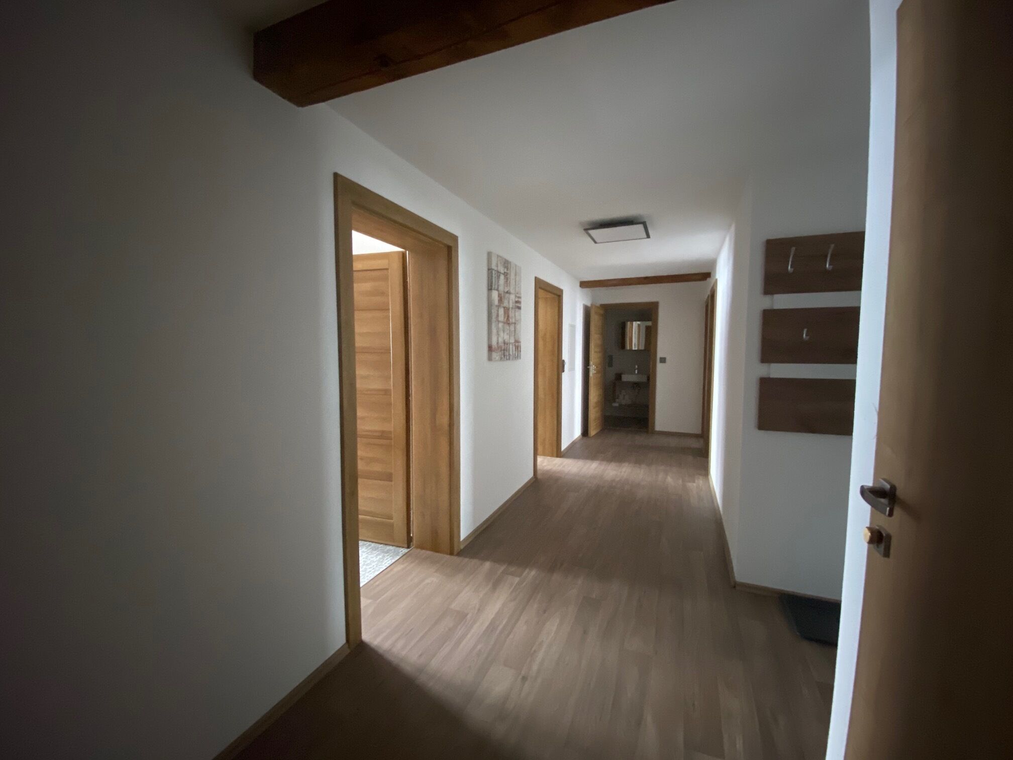 Un pasillo con suelo de madera y puertas, que conduce a una habitación con cama y mesita de noche.