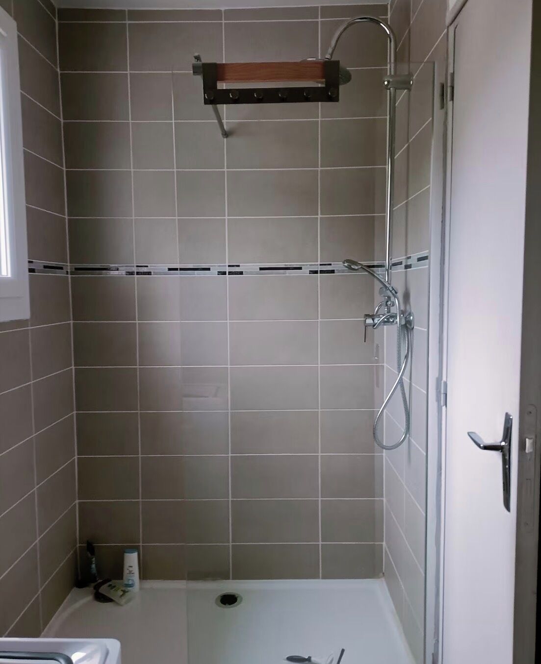 Un espace douche doté d’une porte en verre, d’un pommeau de douche en métal et d’une étagère en bois située au-dessus de la douche.