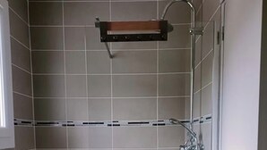 A shower area with a glass door, a metal showerhead, and a wooden shelf above the shower. - A cozy, fully equipped home with a breathtaking view (Vernet-les-Bains)