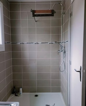 A shower area with a glass door, a metal showerhead, and a wooden shelf above the shower. - A cozy, fully equipped home with a breathtaking view (Vernet-les-Bains)