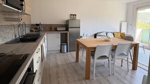A modern kitchen with a built-in oven, a refrigerator, and a dining area with a wooden table and chairs. - A cozy, fully equipped home with a breathtaking view (Vernet-les-Bains)