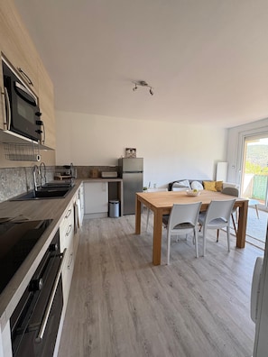 A modern kitchen with a built-in oven, a refrigerator, and a dining area with a wooden table and chairs. - A cozy, fully equipped home with a breathtaking view (Vernet-les-Bains)
