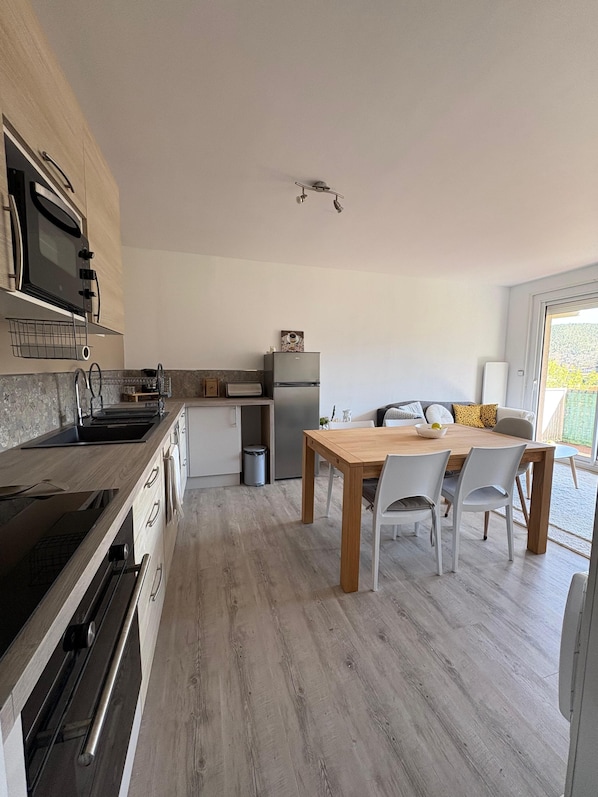 Una cucina moderna con forno integrato, frigorifero e zona pranzo con tavolo e sedie in legno.