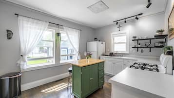 Et moderne køkken med et grønt skab, hvide bordplader og en stålfarvet komfur.