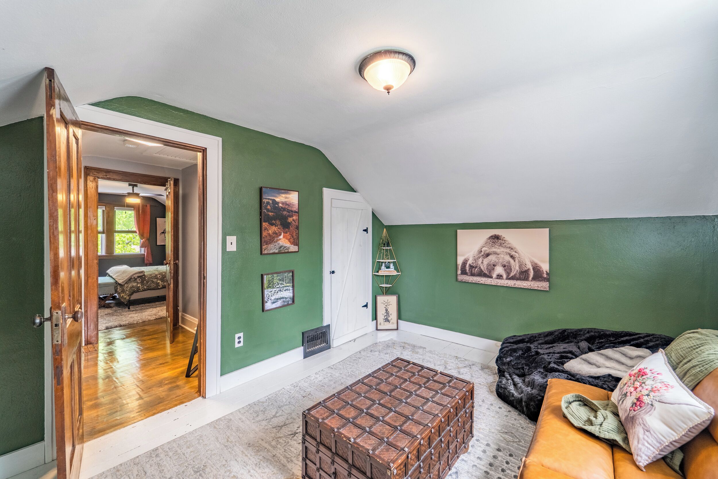 A room with a sloped ceiling, a wooden bench, a cushioned bench, and a door leading to another room.