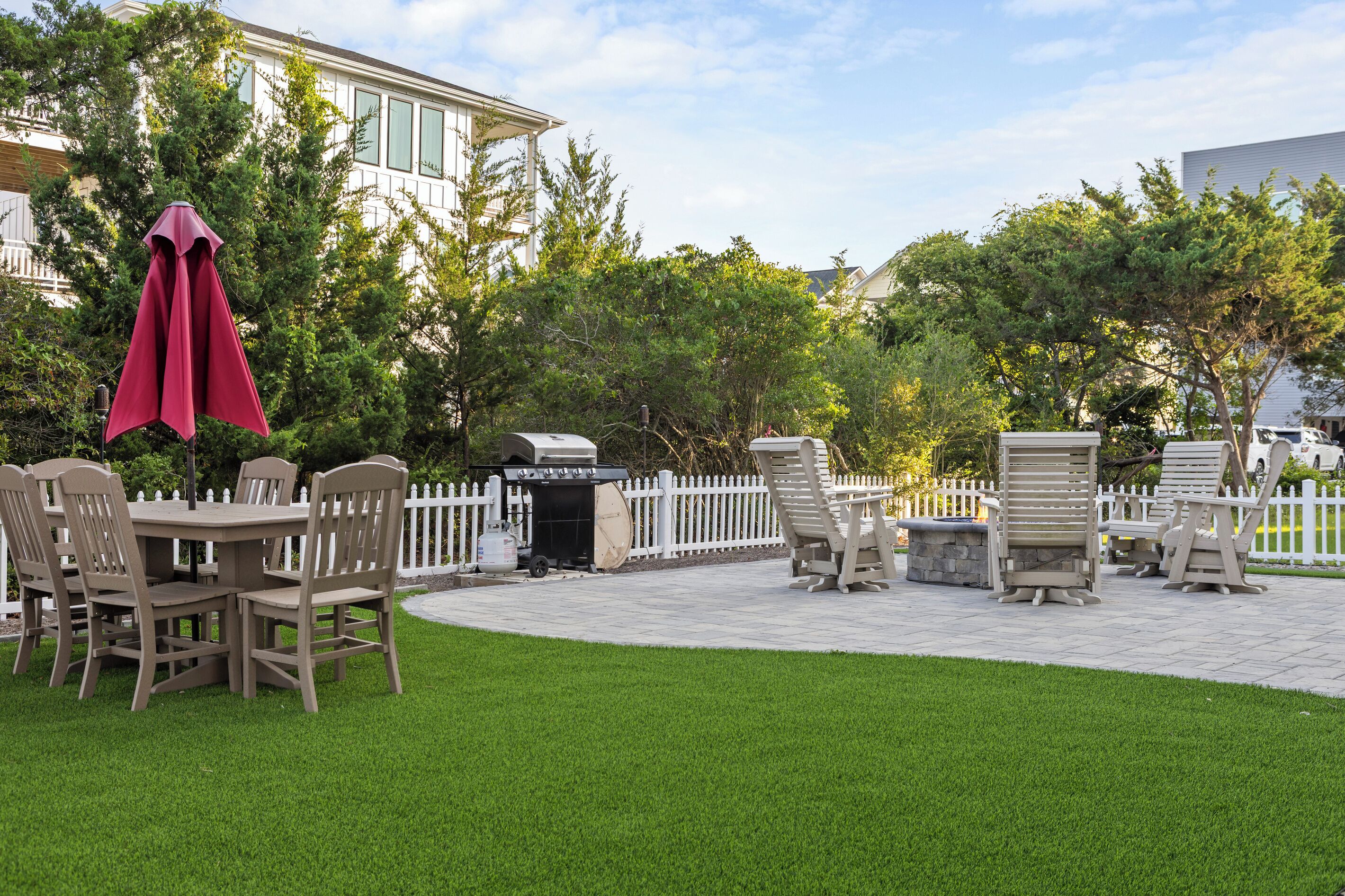 An outdoor patio with a grill, seating, and a white picket fence.