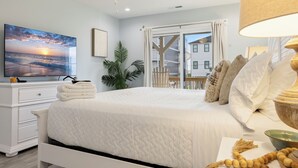 A bedroom with a bed, a TV, a plant, and a view of a building outside. - Ocean Views, Elevator, Fire Pit (Surf City)