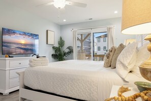 A bedroom with a bed, a TV, a plant, and a view of a building outside. - Ocean Views, Elevator, Fire Pit (Surf City)