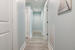 A hallway with white doors, light blue walls, and a wooden floor. - Ocean Views, Elevator, Fire Pit (Surf City)