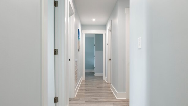A hallway with white walls, wooden flooring, and doors on both sides leading to other rooms. - Ocean Views, Elevator, Fire Pit (Surf City)