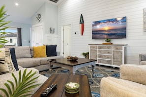 A living room with a sofa, coffee table, and a television displaying a sunset. - Ocean Views, Elevator, Fire Pit (Surf City)