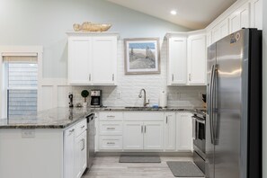 A modern kitchen with white cabinetry, a stainless steel refrigerator, and a coffee maker. - Ocean Views, Elevator, Fire Pit (Surf City)