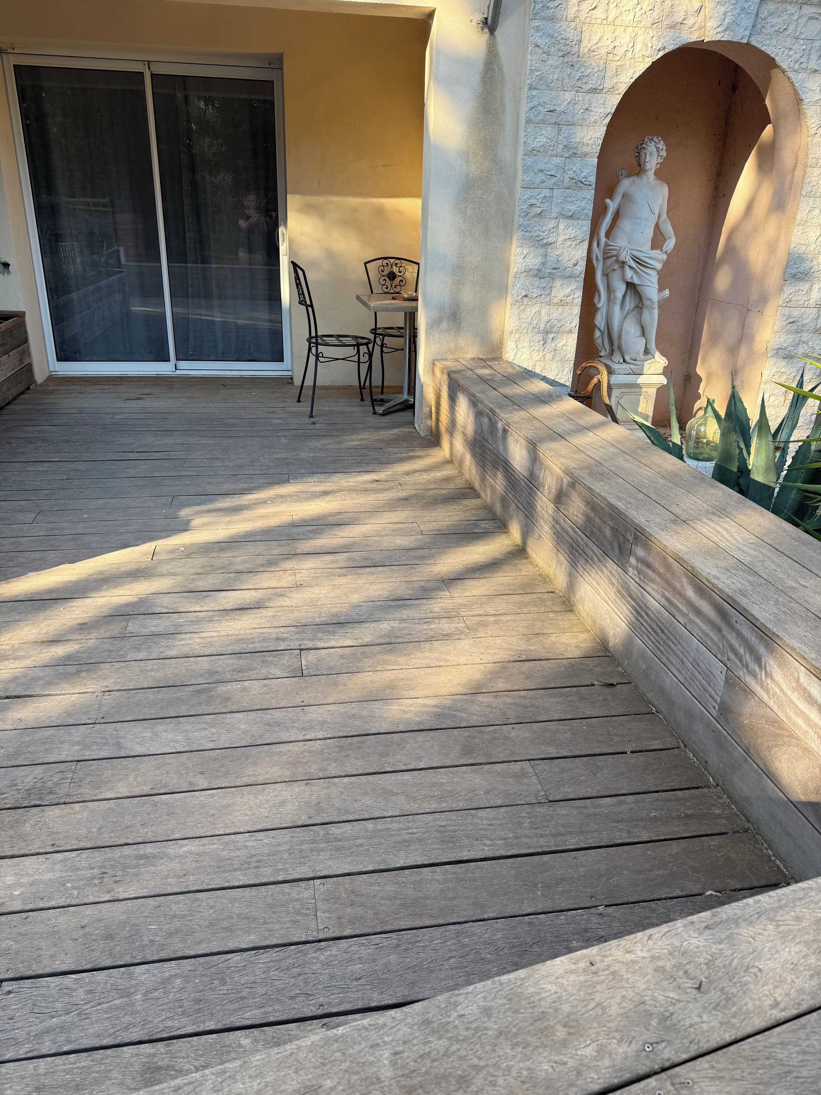 A wooden deck with a statue and a table with chairs.