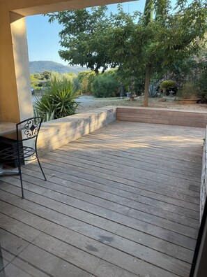 A wooden deck with a metal chair, surrounded by a garden with various plants and a view of hills. - In the heart of Provence, between the sea and the hills (Aubagne)