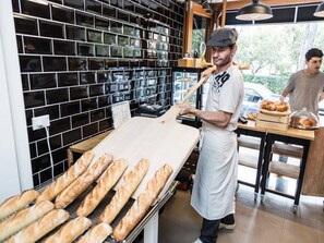 A bakery with a display of baguettes, a person in an apron, and a counter with baked goods. - Stunning Home in the Heart of Surry Hills (Surry Hills)