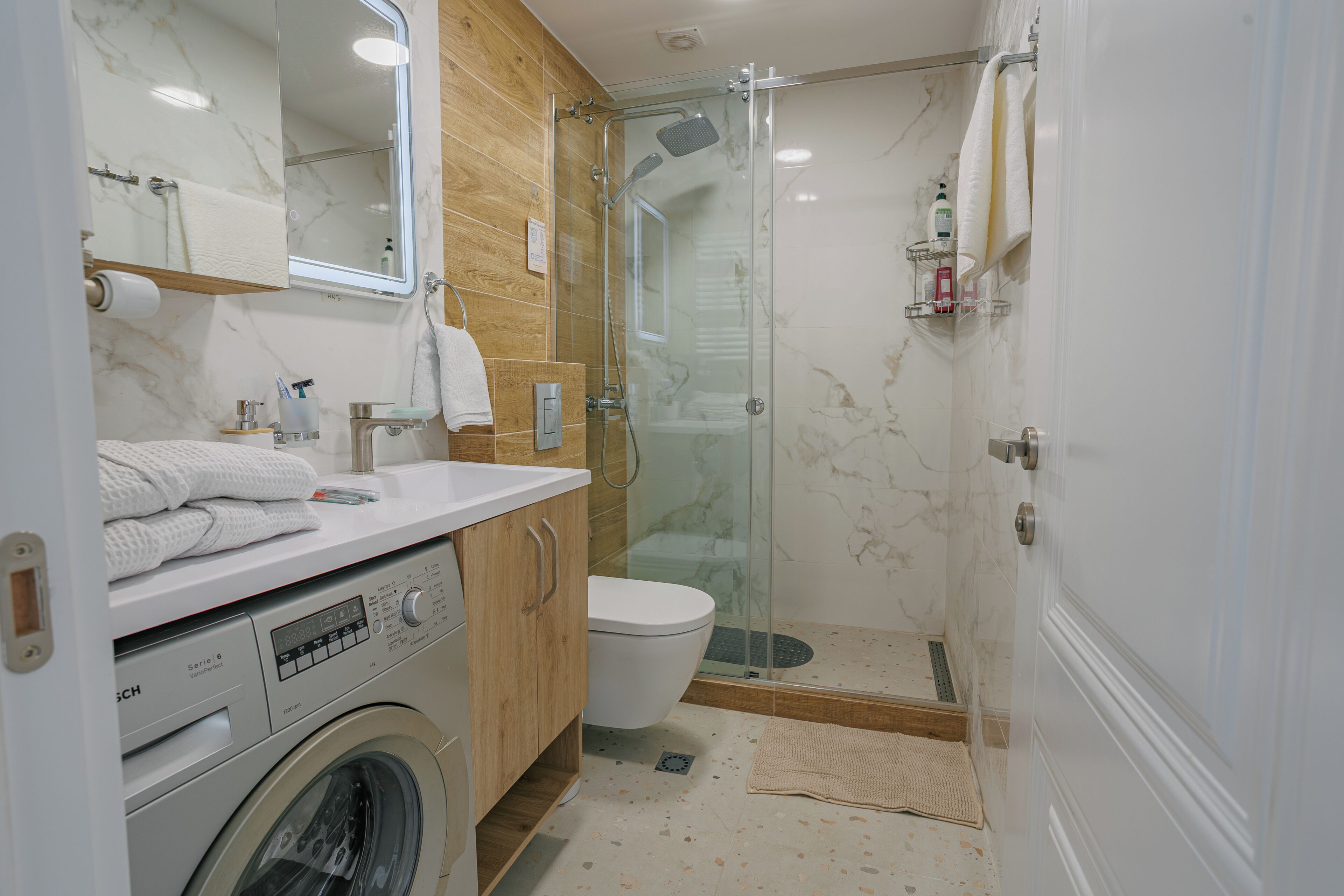 Un baño moderno con ducha de vidrio, lavadora e inodoro.