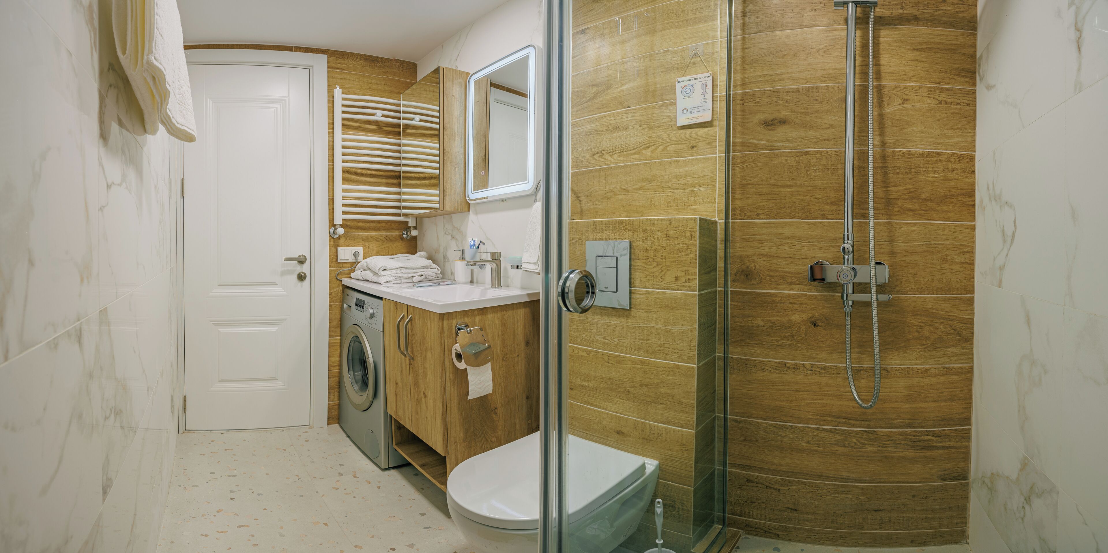 Un bagno moderno con cabina doccia in vetro, lavatrice integrata e un water.