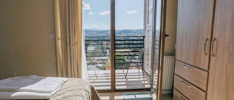 Un dormitorio con cama, armario, balcón y vistas de la ciudad, además de una puerta corrediza de cristal.
