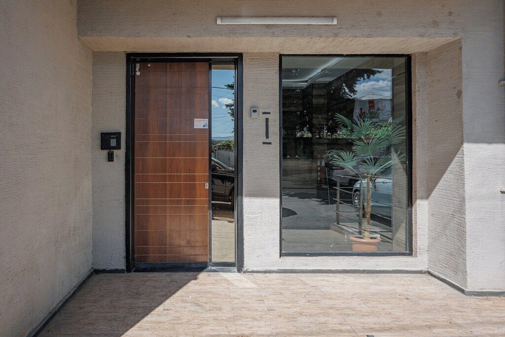 A modern building entrance with a wooden door and a glass door, a potted plant, and a small outdoor area.