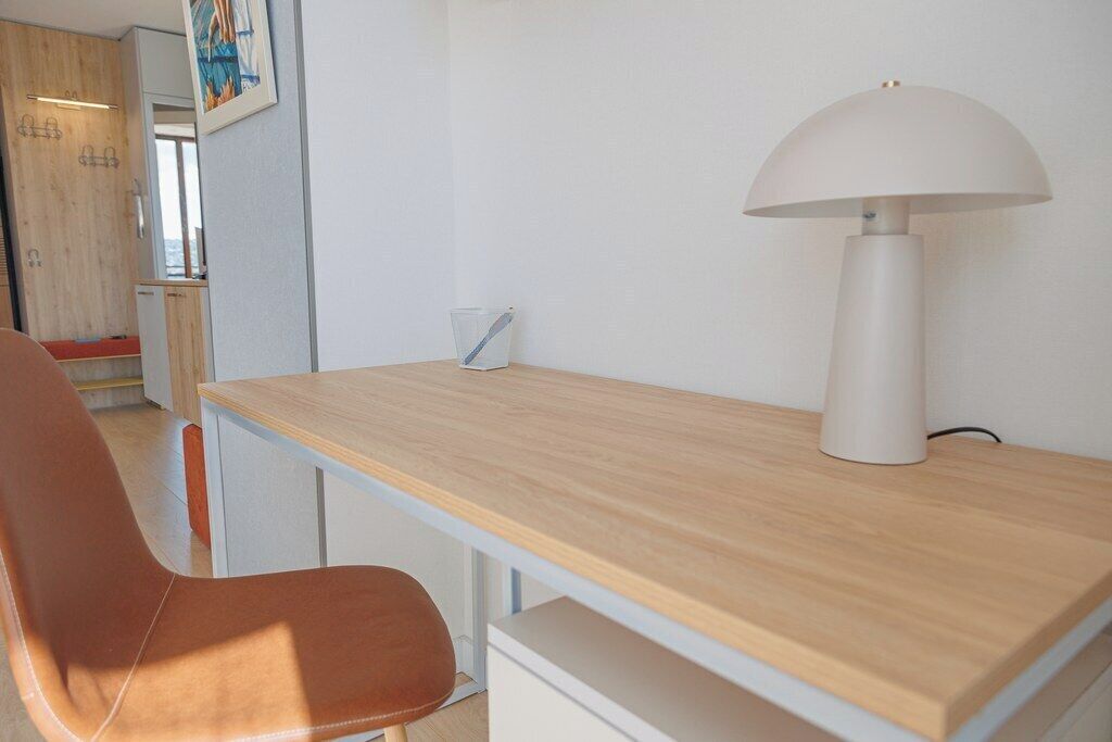 Una habitación con un escritorio de madera, una lámpara blanca y una silla marrón.