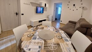 A modern living room with a dining table, a television mounted on the wall, and a clock. - Cozy Apartment in La Spezia—La Spezia's Little Gem (La Spezia)