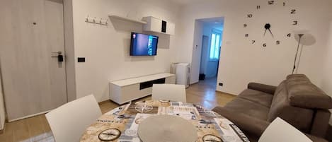 Un soggiorno moderno con un tavolo da pranzo, una televisione a parete e una sveglia.