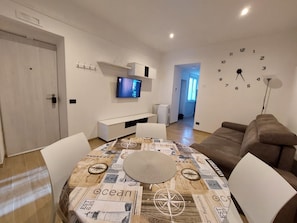 A modern living room with a dining table, a television mounted on the wall, and a clock. - Cozy Apartment in La Spezia—La Spezia's Little Gem (La Spezia)