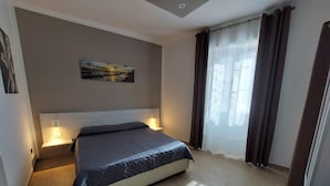 A hotel room with a bed, bedside lamps, a painting on the wall, and a window with curtains. - Cozy Apartment in La Spezia—La Spezia's Little Gem (La Spezia)