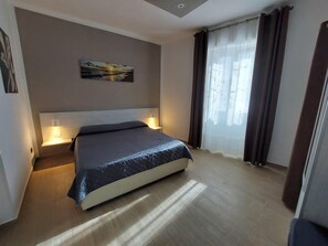 A hotel room with a bed, bedside lamps, a painting on the wall, and a window with curtains. - Cozy Apartment in La Spezia—La Spezia's Little Gem (La Spezia)