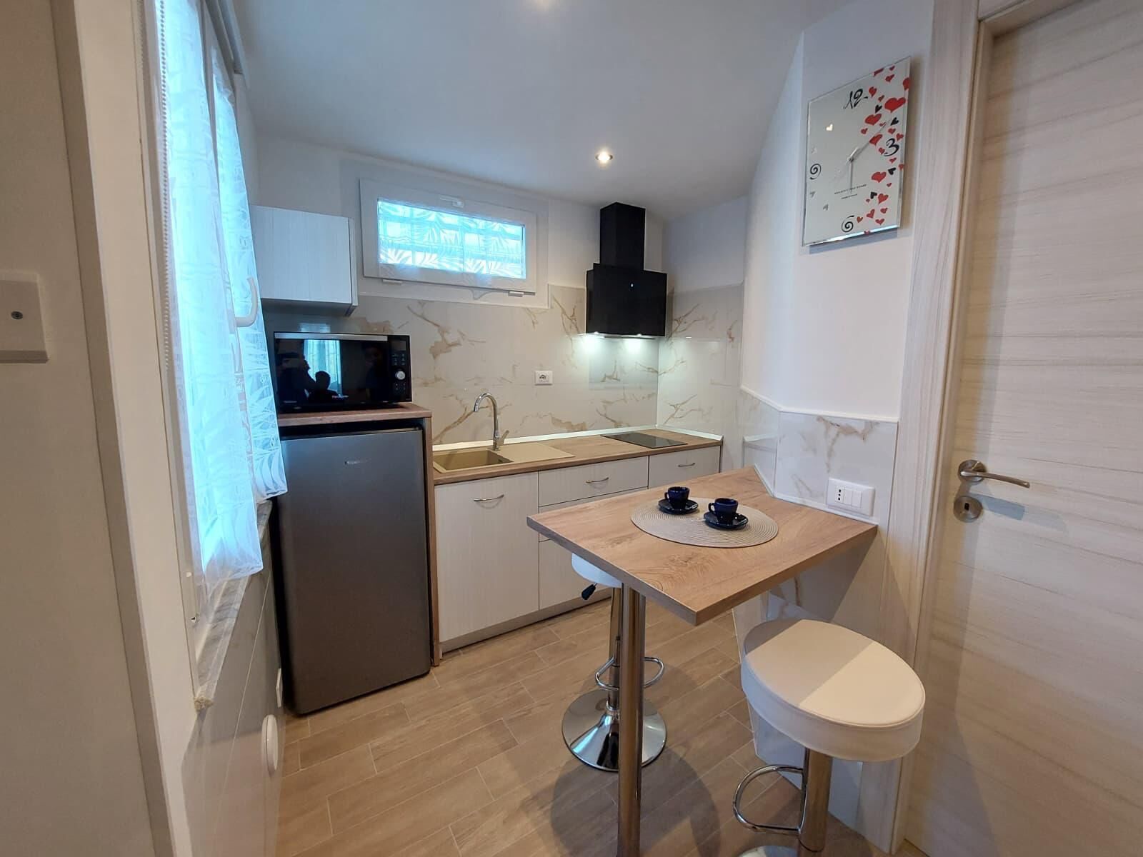 A compact kitchen with a refrigerator, microwave, sink, and a small table with two cups.