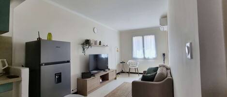 A compact living space with a kitchenette, a flat-screen TV, a sofa, and a small dining table.