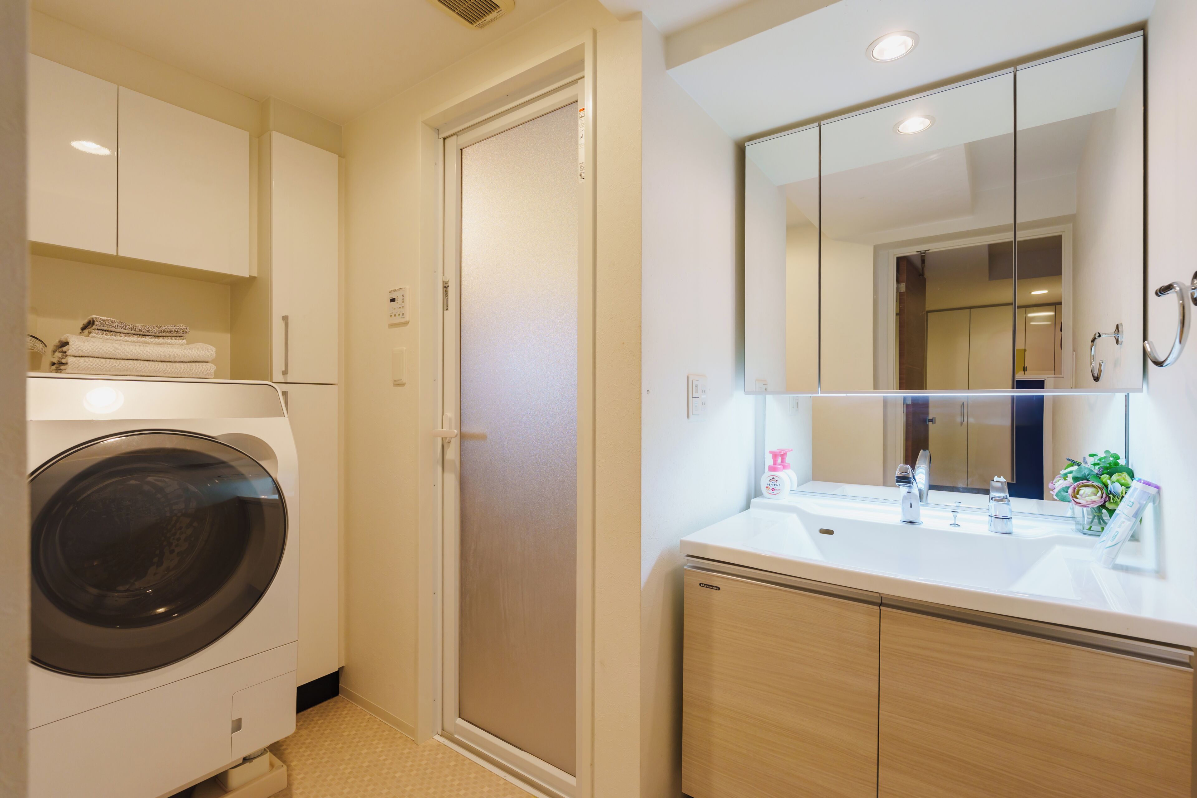 A compact hotel bathroom with a washing machine, a shower, and a sink with a mirror.