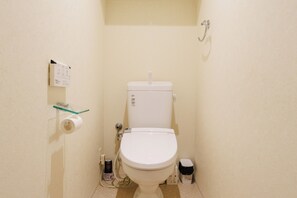 A small, compact bathroom with a white toilet, a glass shelf with a roll of toilet paper, and a trash bin.