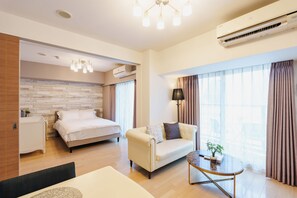 A modern hotel room with a bed, a sofa, a small table, and an air conditioning unit. - SERENE | Kuromon · 1006 | 60 m² · 2BR | Sleeps 6 | Family Suite | 2 min to Kuromon (大阪市)