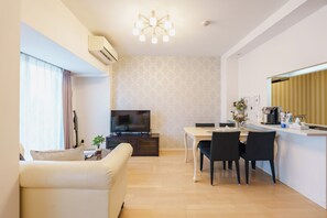 A modern living room with a flat-screen TV, a dining area with a table and chairs, and a kitchen area with a countertop and appliances.