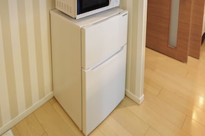 A white refrigerator with a microwave on top, located in a corner of a room with wooden flooring and striped wallpaper. - SERENE | Kuromon · 1006 | 60 m² · 2BR | Sleeps 6 | Family Suite | 2 min to Kuromon (大阪市)