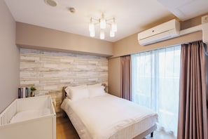 A bedroom with a bed, a crib, a brick-patterned wall, an air conditioning unit, and a window with curtains.