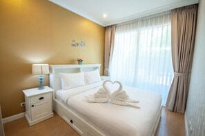 Ein Hotelzimmer mit Bett, Nachttisch, Lampe, Wanddeko und einem Fenster mit Vorhängen.