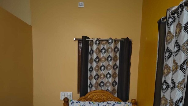 Una cama individual con una colcha estampada, cabecera de madera y una ventana con cortina decorada.
