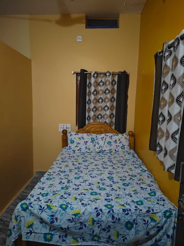 A single bed with a floral bedspread, a wooden headboard, and a window with a patterned curtain.